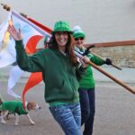 Two adults and a dog wearing green waving from a parade